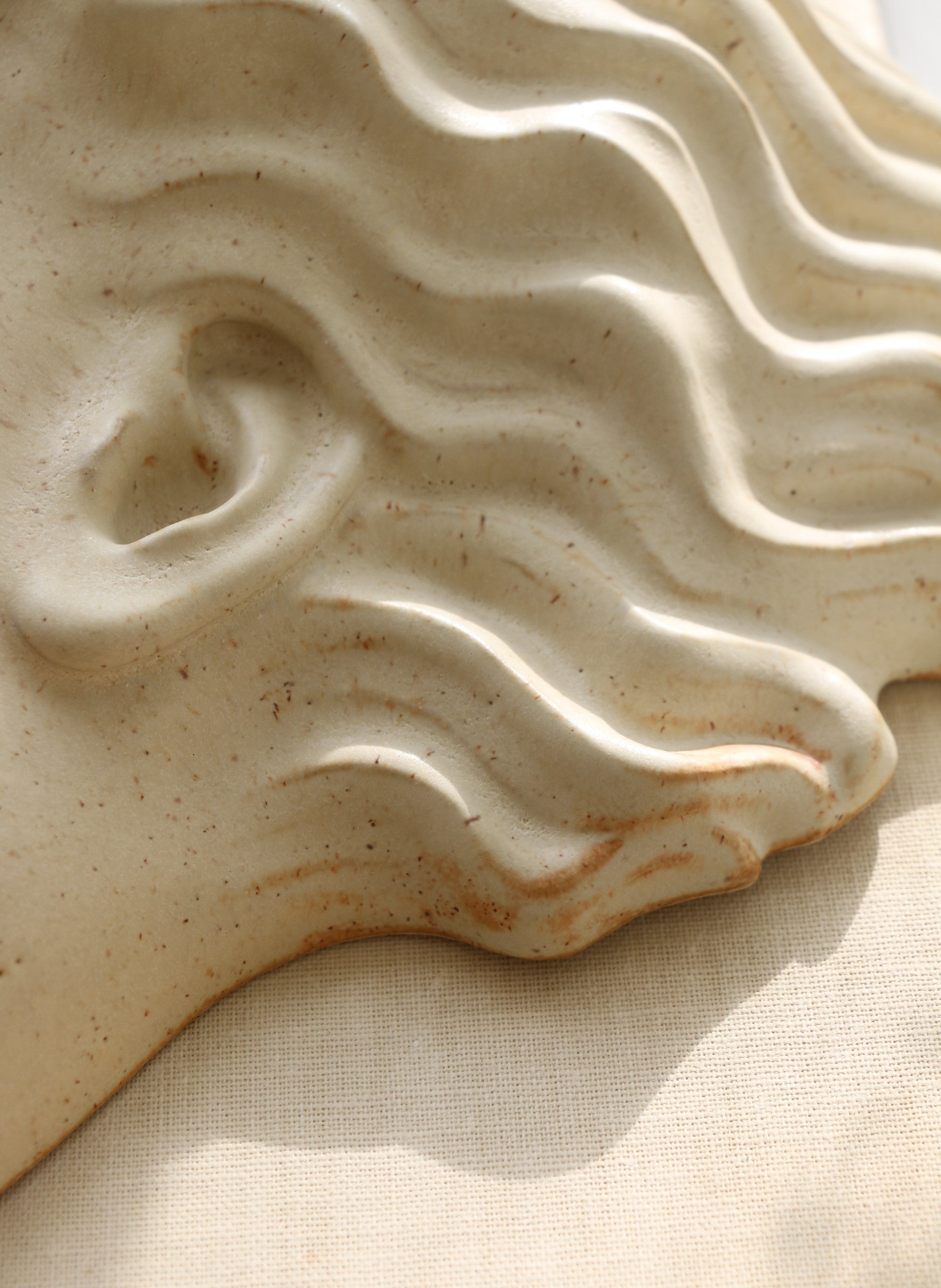 Handmade ceramic mask Hera by Laoru Laoru, close-up detail of sculpted ear and wavy hair in Warm Sand glazed stoneware.
